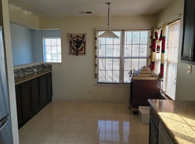 kitchen with light stone counters, light tile patterned flooring, backsplash, and hanging light fixtures