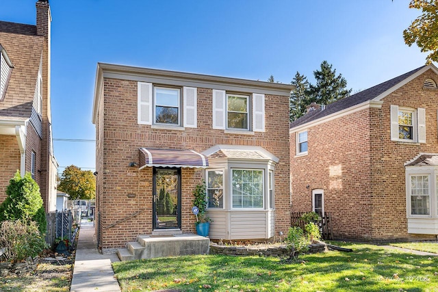 traditional-style house featuring brick siding, a front lawn, and fence