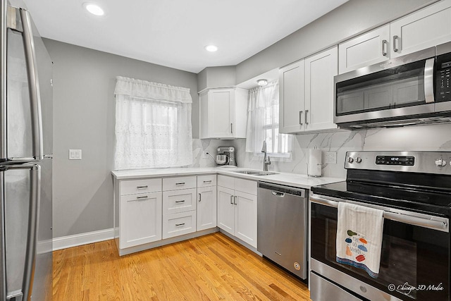 kitchen with a sink, white cabinetry, appliances with stainless steel finishes, light wood finished floors, and light countertops