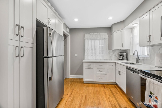 kitchen with light wood-type flooring, light countertops, appliances with stainless steel finishes, white cabinets, and a sink