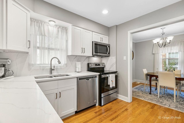 kitchen with light stone countertops, a sink, stainless steel appliances, light wood-style floors, and white cabinetry