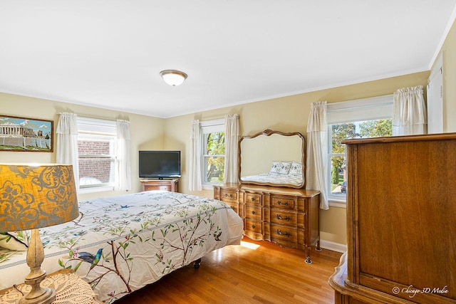 bedroom with multiple windows, wood finished floors, baseboards, and ornamental molding