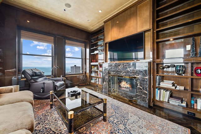 living room featuring a fireplace, crown molding, built in features, and wooden walls