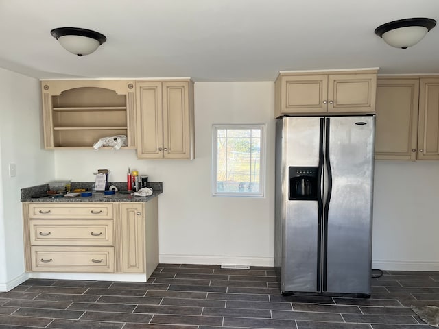 kitchen featuring cream cabinetry, stainless steel fridge, dark stone countertops, and dark wood-type flooring