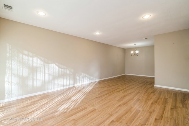 unfurnished room featuring an inviting chandelier and light wood-type flooring