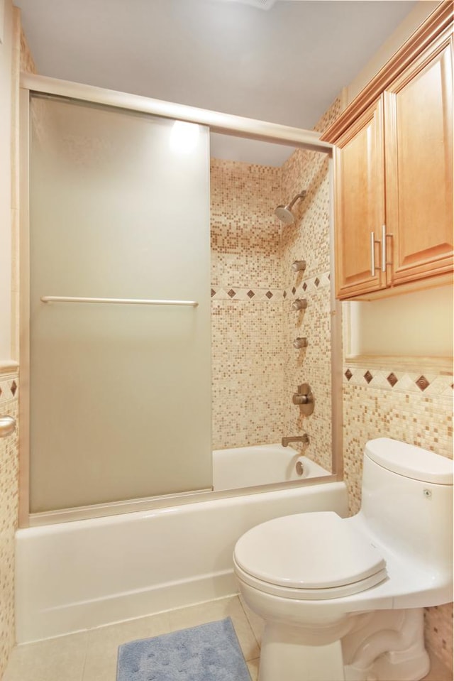 830 E 191st Pl Unit 709, Glenwood, IL 60425 - full bath featuring tile patterned flooring, tile walls, toilet, bath / shower combo with glass door, and a wainscoted wall