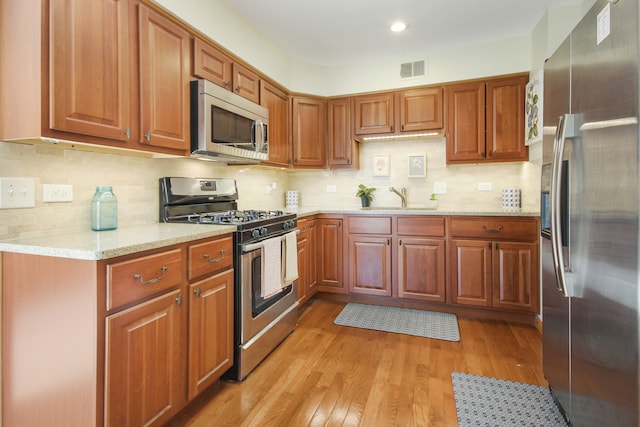 kitchen with decorative backsplash, appliances with stainless steel finishes, light stone counters, sink, and light hardwood / wood-style flooring