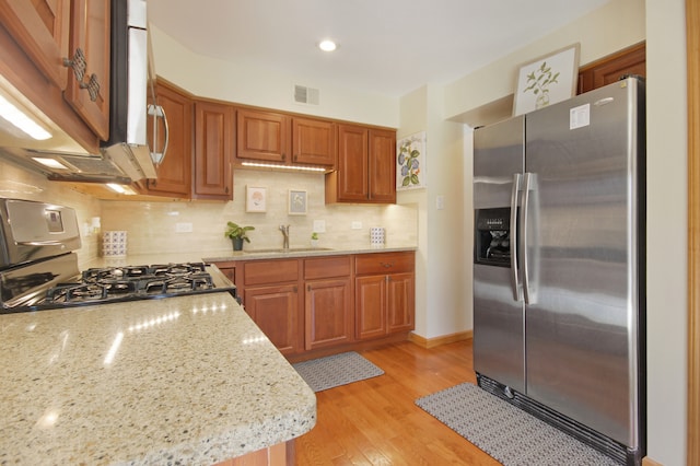 kitchen featuring backsplash, sink, appliances with stainless steel finishes, light hardwood / wood-style floors, and light stone counters