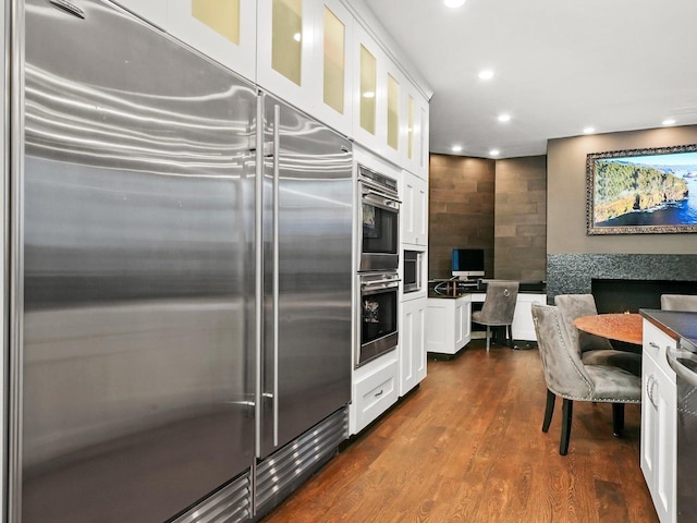 kitchen with appliances with stainless steel finishes, dark wood-type flooring, built in desk, and white cabinets