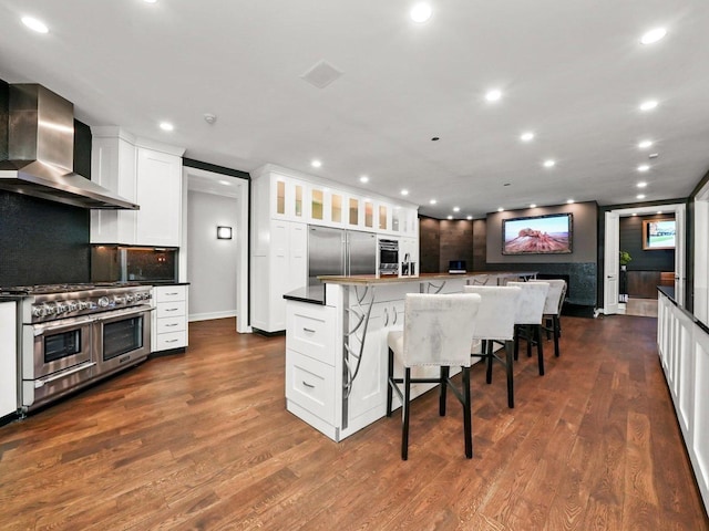 kitchen featuring dark wood-type flooring, a kitchen breakfast bar, high end appliances, white cabinets, and wall chimney exhaust hood