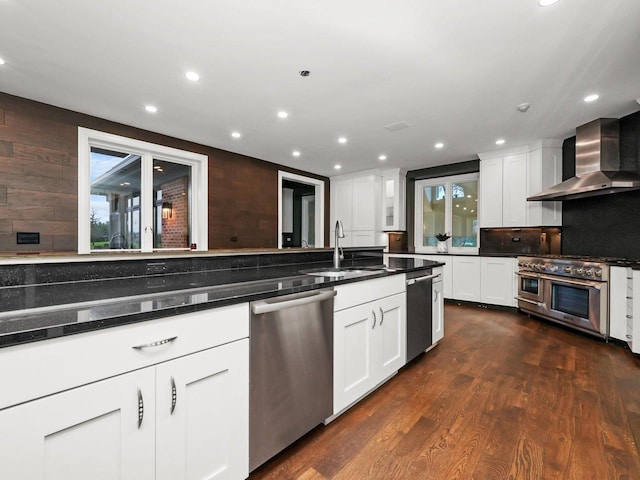 kitchen with wall chimney exhaust hood, sink, stainless steel dishwasher, wall oven, and white cabinets