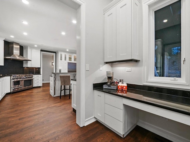 kitchen featuring built in desk, white cabinets, range with two ovens, dark wood-type flooring, and wall chimney exhaust hood