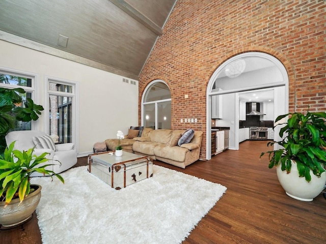 living room featuring dark wood-type flooring, high vaulted ceiling, and brick wall