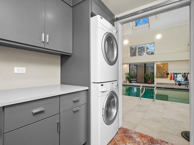 clothes washing area featuring stacked washer / drying machine, light tile patterned floors, and cabinets