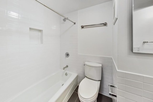 bathroom featuring toilet, tile walls, and tiled shower / bath