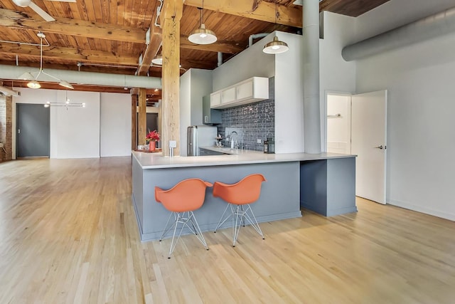 kitchen with kitchen peninsula, sink, pendant lighting, beamed ceiling, and white cabinets