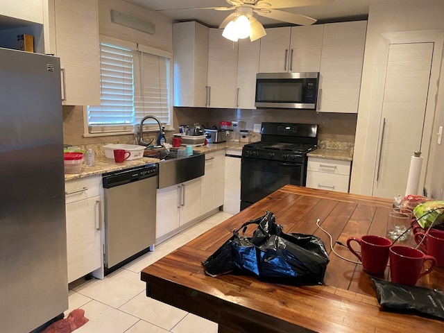 kitchen featuring sink, light tile patterned floors, light stone countertops, appliances with stainless steel finishes, and white cabinetry