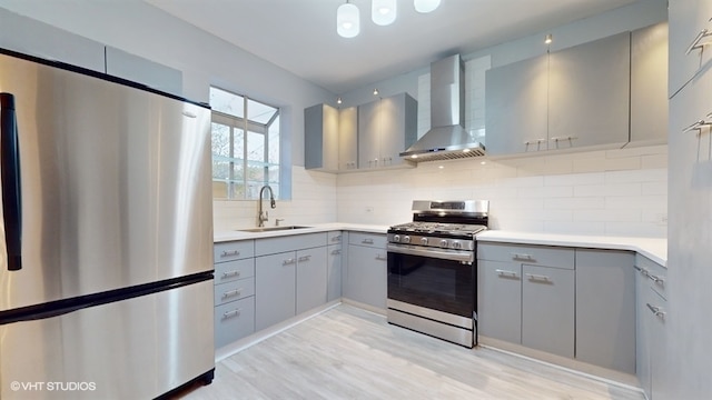 kitchen with sink, light hardwood / wood-style flooring, wall chimney exhaust hood, appliances with stainless steel finishes, and tasteful backsplash