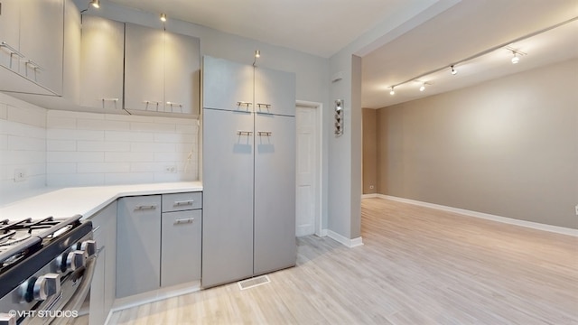 kitchen featuring stainless steel gas stove, gray cabinets, light hardwood / wood-style floors, and tasteful backsplash