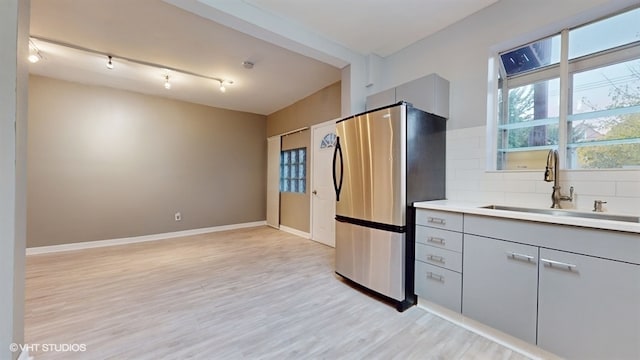 kitchen featuring sink, light hardwood / wood-style flooring, gray cabinets, tasteful backsplash, and stainless steel refrigerator