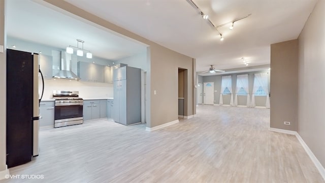 kitchen with hanging light fixtures, wall chimney exhaust hood, light wood-type flooring, and stainless steel gas range