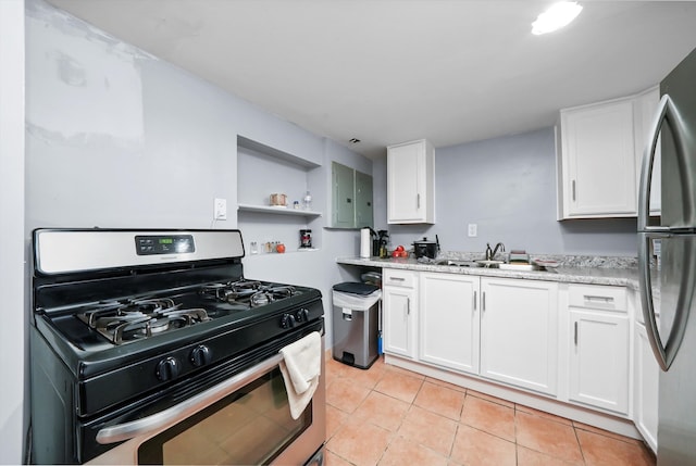 kitchen featuring gas range, sink, light tile patterned floors, white cabinetry, and stainless steel refrigerator