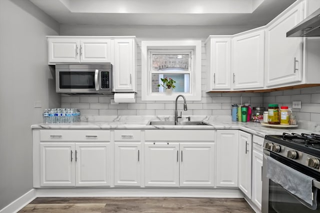 kitchen featuring stainless steel appliances, white cabinetry, wall chimney exhaust hood, and sink