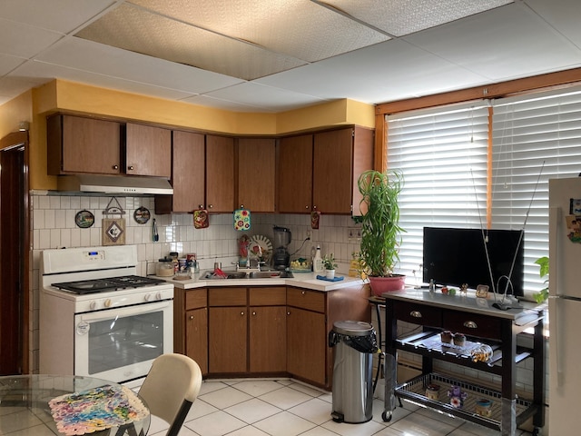 kitchen featuring sink, tasteful backsplash, white appliances, a paneled ceiling, and light tile patterned floors