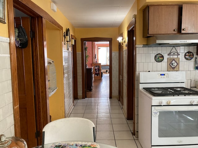 kitchen with light tile patterned floors, tile walls, gas range gas stove, and exhaust hood