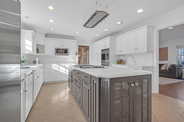 kitchen with crown molding, built in appliances, a center island, light stone countertops, and white cabinets