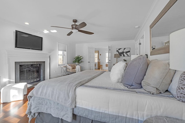 bedroom featuring a tile fireplace, ornamental molding, hardwood / wood-style floors, and ceiling fan