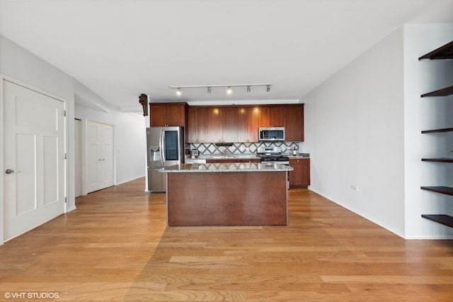 kitchen with light stone countertops, backsplash, light hardwood / wood-style floors, a kitchen island, and appliances with stainless steel finishes