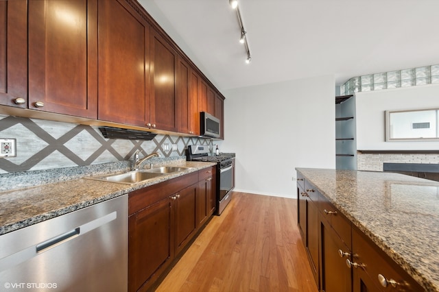 kitchen with sink, light wood-type flooring, appliances with stainless steel finishes, tasteful backsplash, and stone countertops