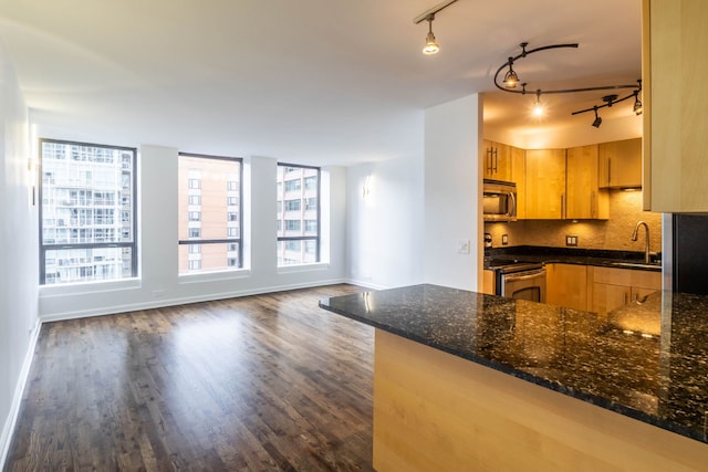 kitchen featuring rail lighting, stainless steel appliances, dark wood-type flooring, light brown cabinets, and dark stone countertops