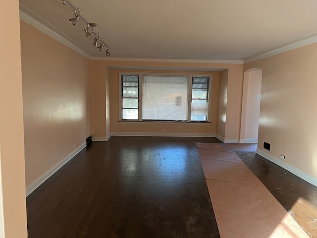 empty room with dark hardwood / wood-style floors, track lighting, and crown molding