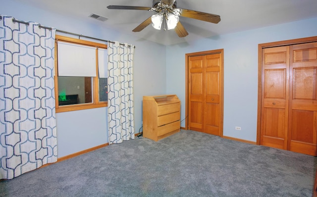 unfurnished bedroom featuring ceiling fan, dark carpet, and two closets