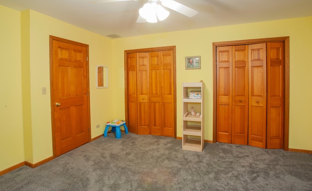 unfurnished bedroom featuring dark colored carpet, ceiling fan, and multiple closets