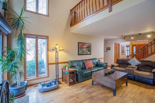 living room with rail lighting, plenty of natural light, a towering ceiling, and light wood-type flooring