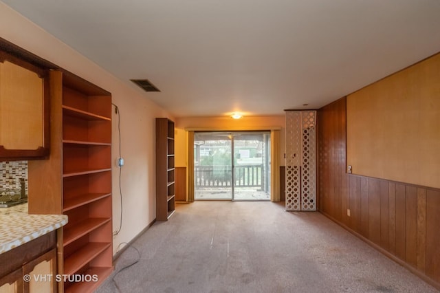 unfurnished living room with light colored carpet and wooden walls