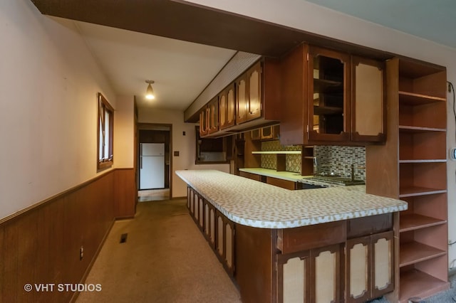 kitchen with kitchen peninsula, backsplash, light colored carpet, wooden walls, and white refrigerator