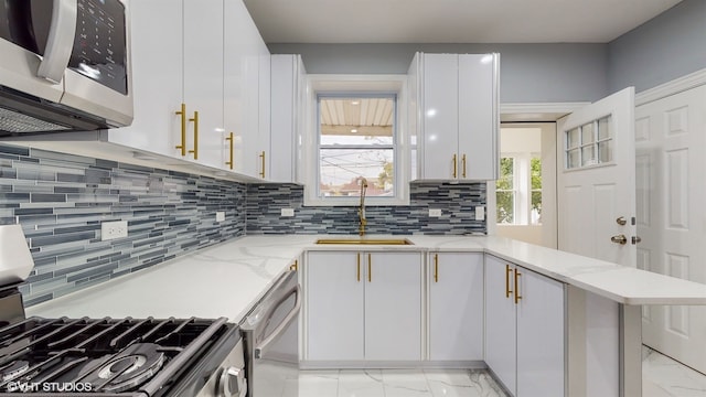 kitchen with white cabinetry, sink, kitchen peninsula, decorative backsplash, and appliances with stainless steel finishes