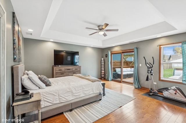 bedroom featuring a tray ceiling, ceiling fan, light hardwood / wood-style floors, and access to outside