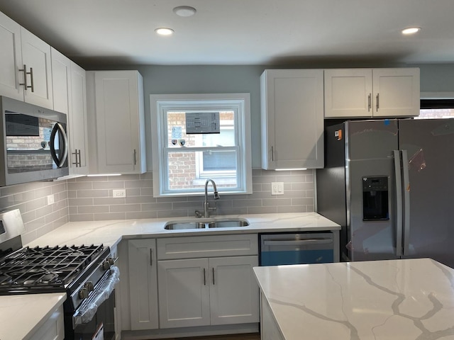 kitchen with sink, decorative backsplash, light stone countertops, appliances with stainless steel finishes, and white cabinetry