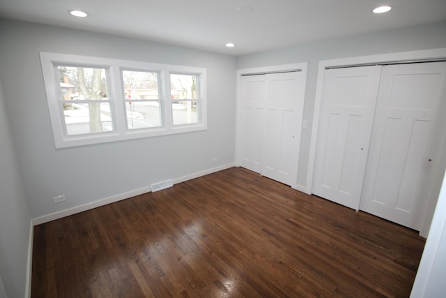 unfurnished bedroom with multiple closets and dark hardwood / wood-style floors