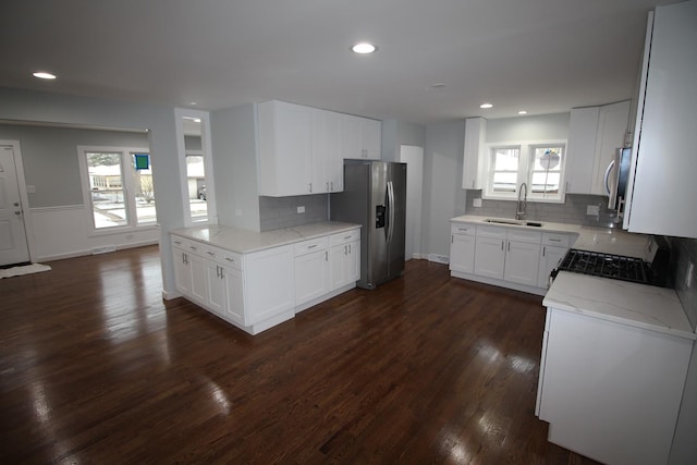 kitchen with white cabinetry, sink, black gas range oven, stainless steel fridge with ice dispenser, and light stone counters