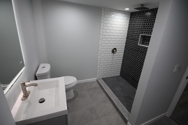 bathroom featuring a tile shower, vanity, and toilet