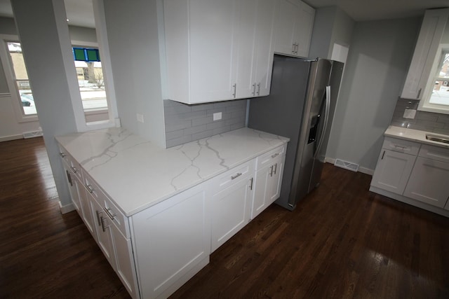 kitchen with white cabinets, decorative backsplash, stainless steel fridge, and light stone counters