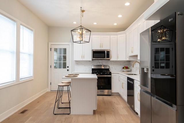 kitchen featuring hanging light fixtures, sink, appliances with stainless steel finishes, a kitchen island, and white cabinetry