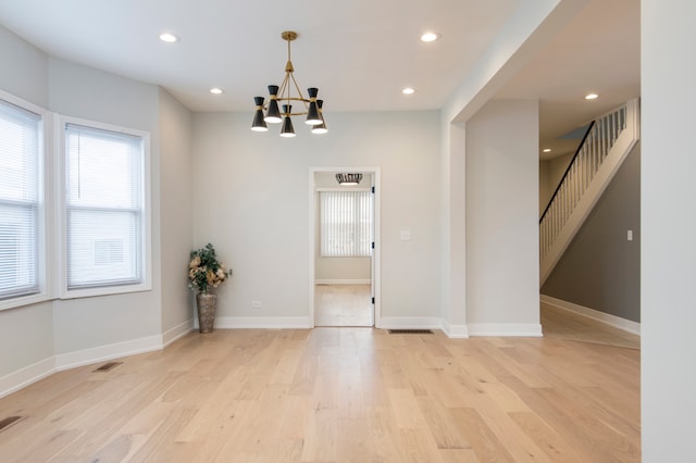 spare room with a chandelier and light wood-type flooring