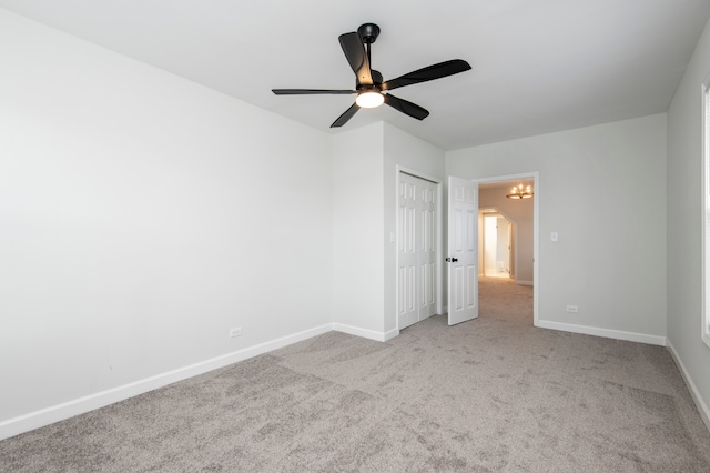 empty room with light colored carpet and ceiling fan with notable chandelier